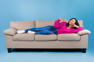 Happy young black woman lying on sofa, feeling hot, waving at herself, mockup f, a Photo by Prostock-Studio