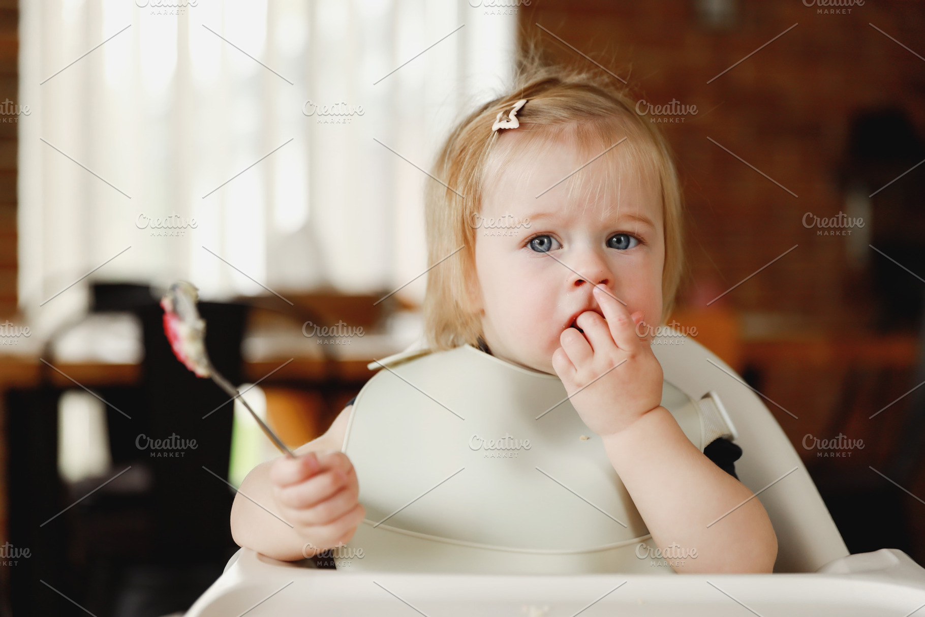 Infant girl or toddler sitting on high chair. Eating food by herself using spoo, a Person Photo by Lenor4ik