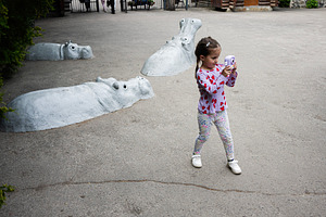 Young girl with camera captures view near submerged hippo sculptures outdoors, a Photo by AS photostudio