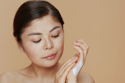 modern asian female with hand cream on beige background, a Person Photo by Alliance Images