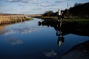 Two children standing on a small wooden dock by a calm river with reflections i, a Person Photo by AS photostudio