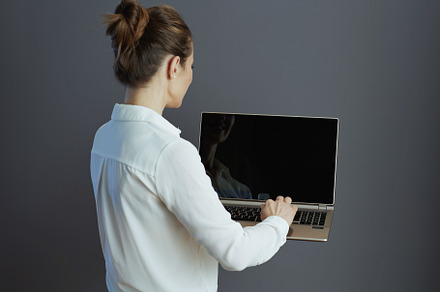 Seen from behind woman worker using laptop isolated on gray, a Business Photo by Alliance Images
