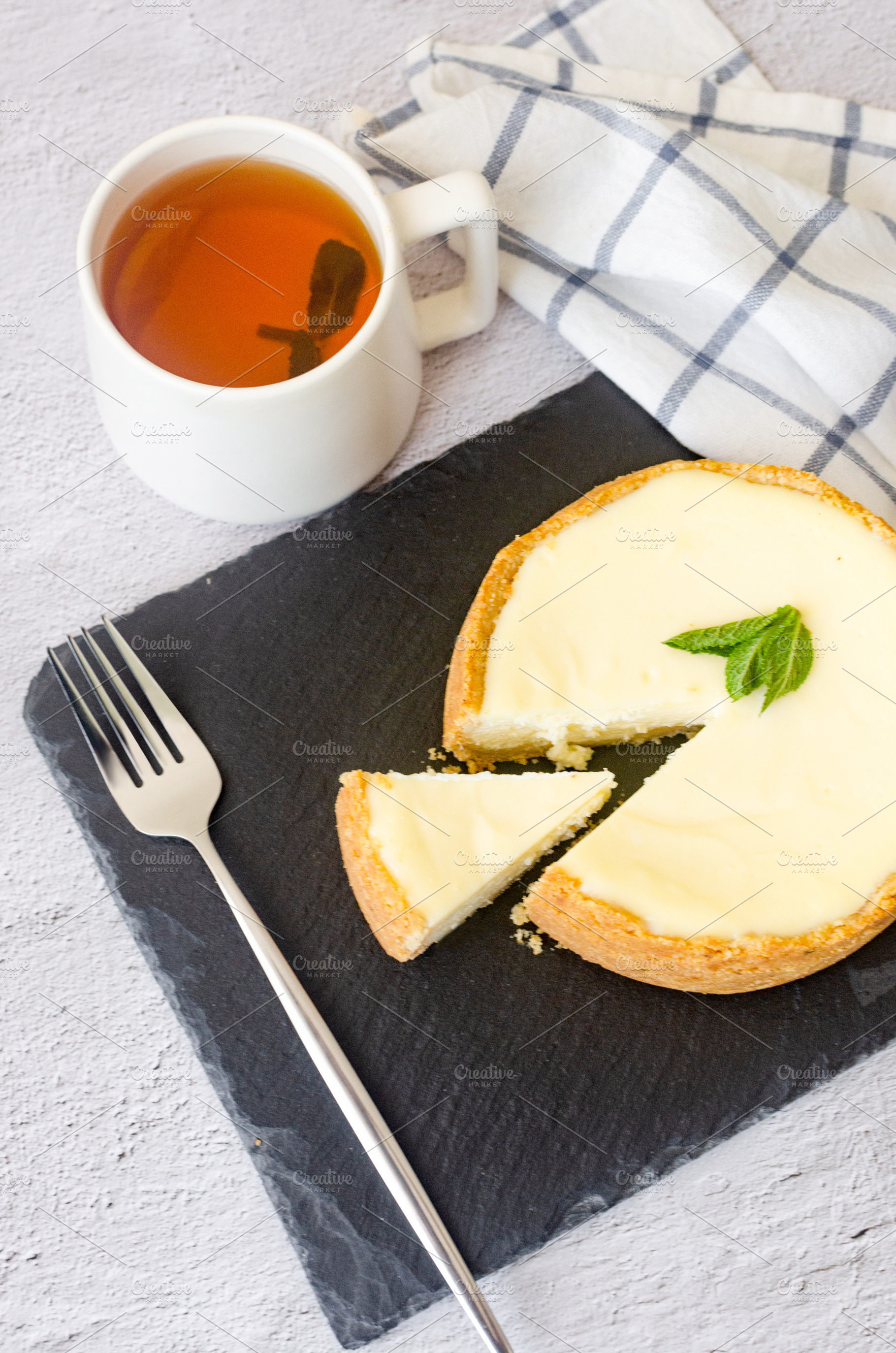 Classic cheesecake with mint leaf and cup of tea on black slate, a Food & Drink Photo by vimart