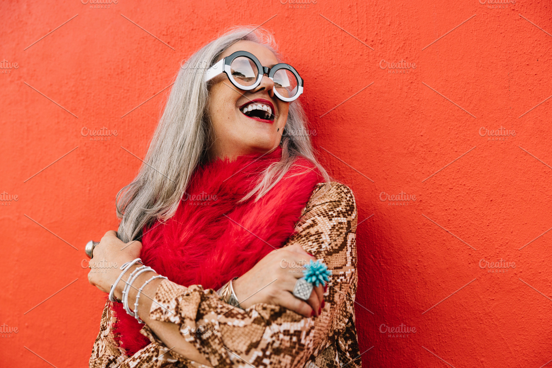 Cheerful senior woman laughing happily against a red wall, a Person Photo by Jacob Lund