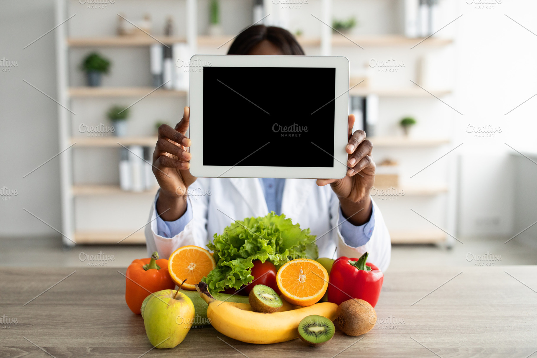 Black nutritionist holding digital tablet with blank screen, demonstrating mock, a Person Photo by Prostock-Studio
