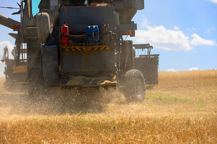 Close-up rear view of a combine harvester spreading straw and du, an Industrial Photo by Ales Munt
