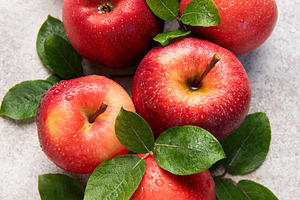 Fresh red apples with green leaves resting on gray surface, a Food & Drink Photo by Olena Rudo