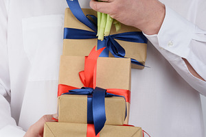 A man in a white shirt holds a stack of craft-wrapped gifts tied, a Person Photo by ndanko