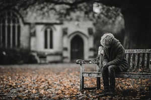 Lonely elderly woman sitting on a park bench outside an old church in autumn, a, a Photo by AS photostudio