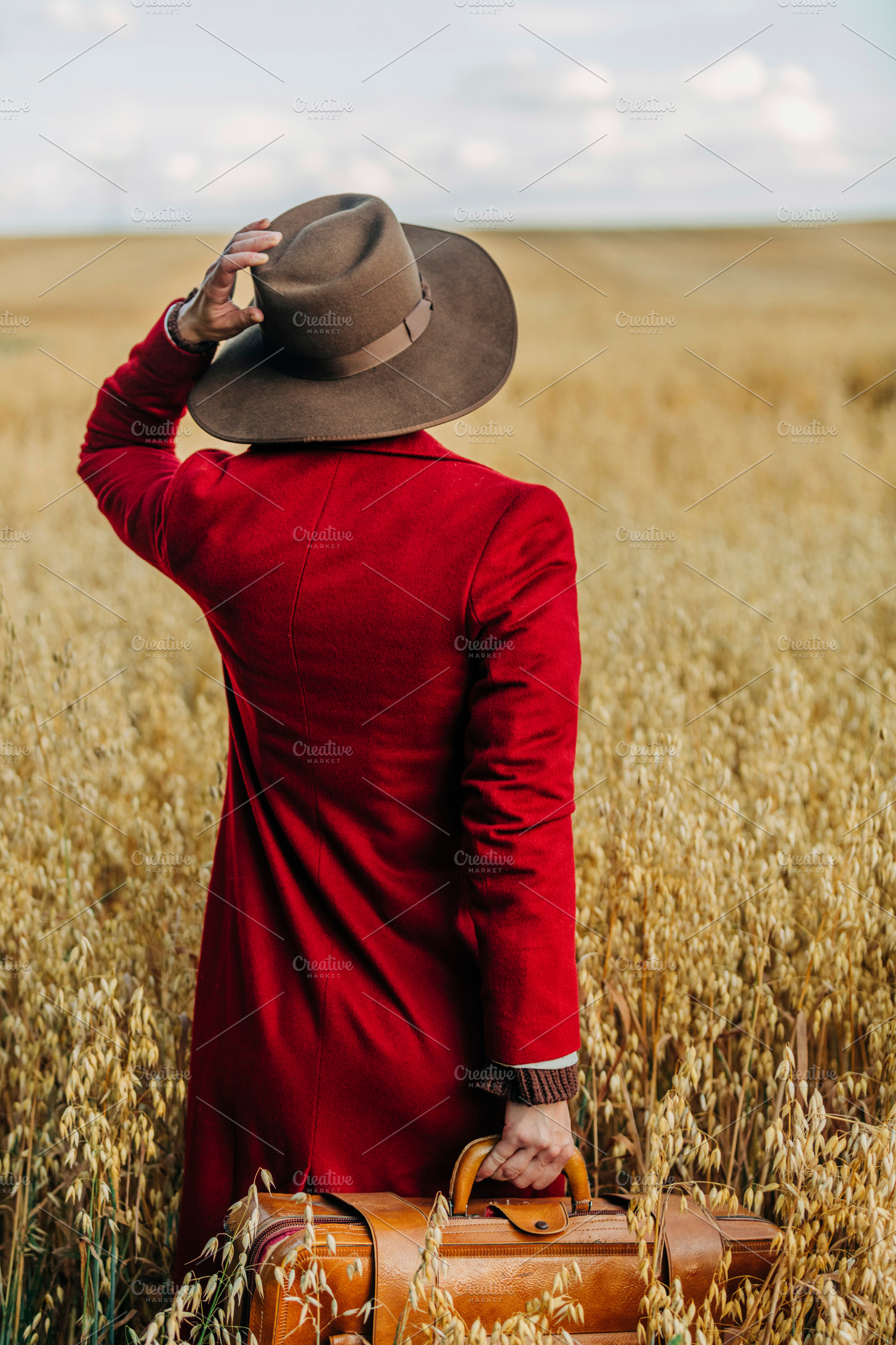 Stylish woman in vintage hat red coat with suitcase on oat field, a Person Photo by Masson Simon