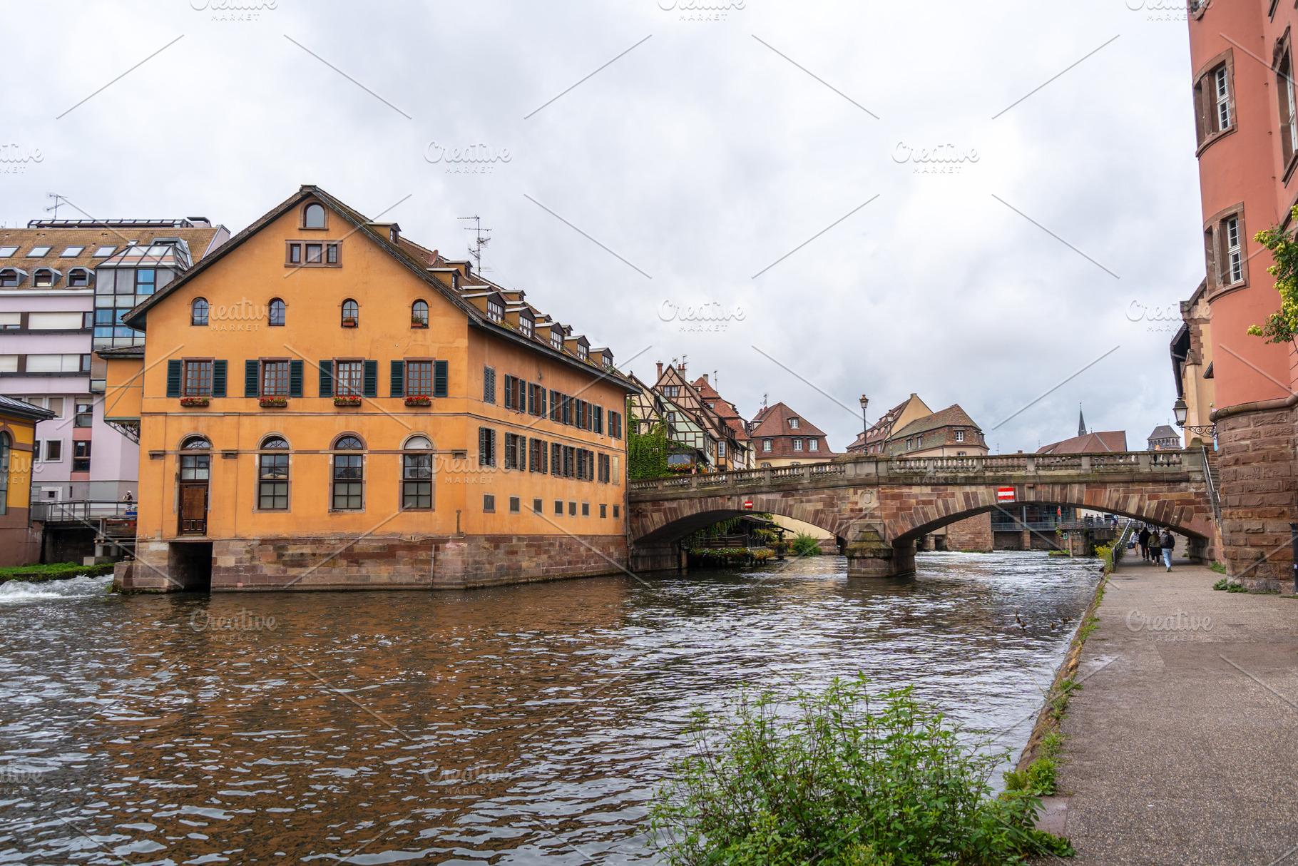 Yellow riverside building and stone bridge in Strasbourg, France, an Architecture Photo by GoodGoods
