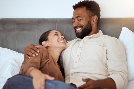 Love, relax and couple in bed in their home, resting and smiling while talking and bonding in bedroom together. Black family, resting and comfort with smile, happy and laughing man and woman embrace, a Photo by Peopleimages.com