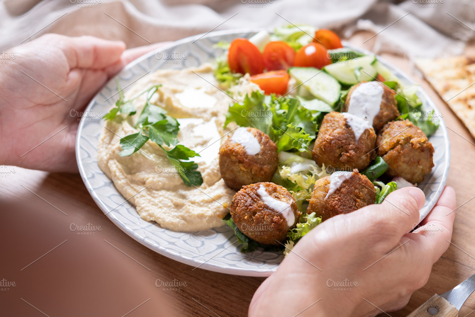 Person holding plate of falafel with hummus and fresh salad, a Food & Drink Photo by etorres69