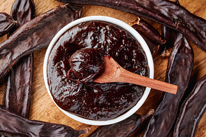 carob cream in a bowl and pods on a wooden table, a Photo by Nito