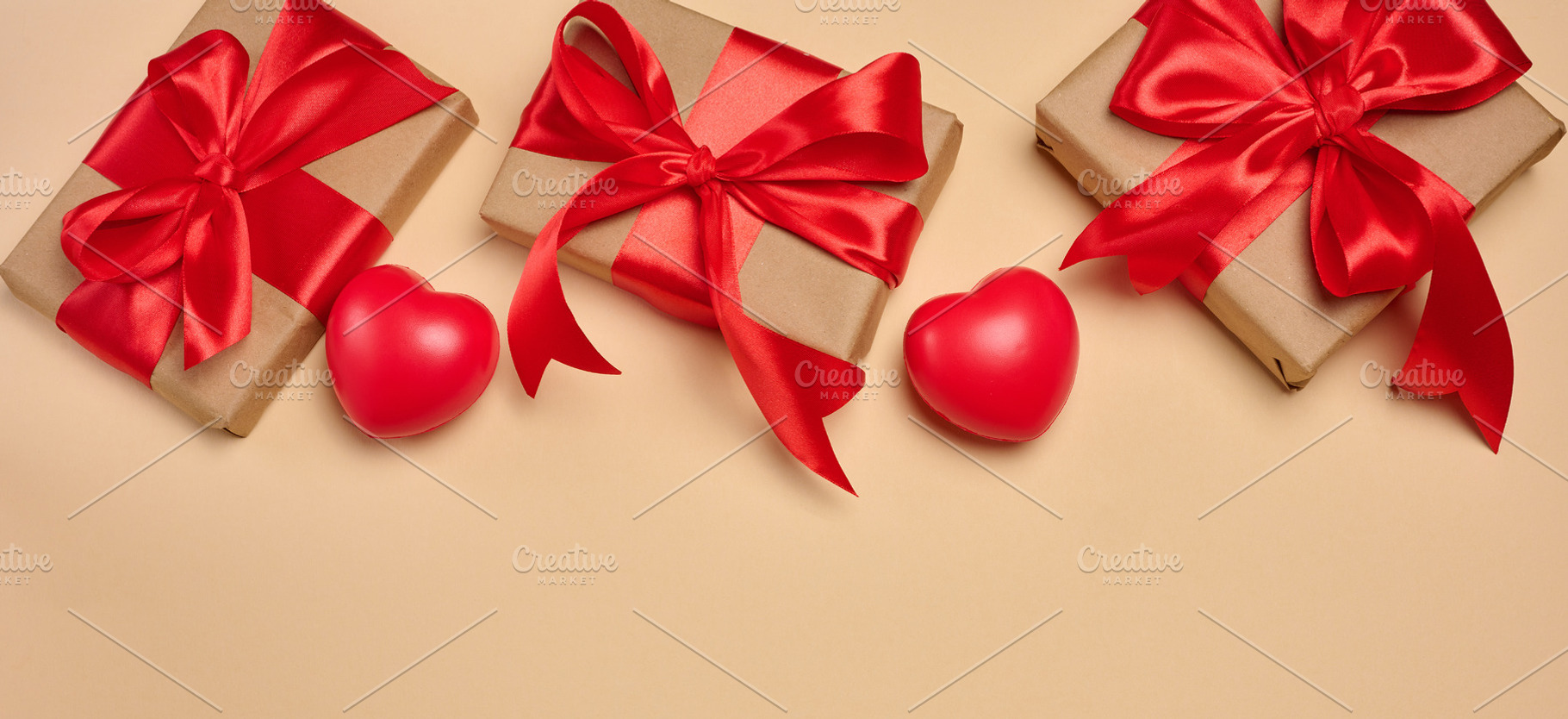 Gifts wrapped in red satin ribbon with a bow on a beige backgrou, a Holiday Photo by ndanko