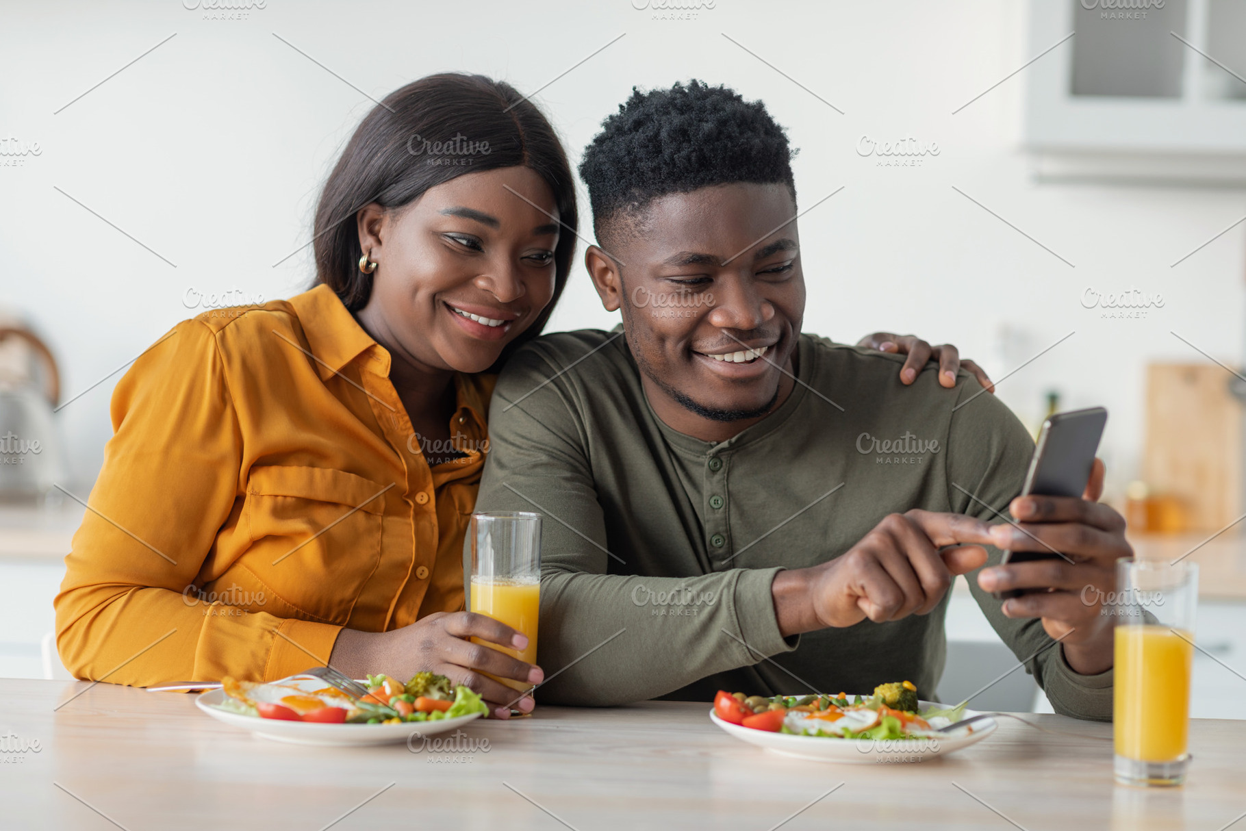 Happy African American Couple Relaxing With Smartphone While Having Breakfast I, a Photo by Prostock-Studio