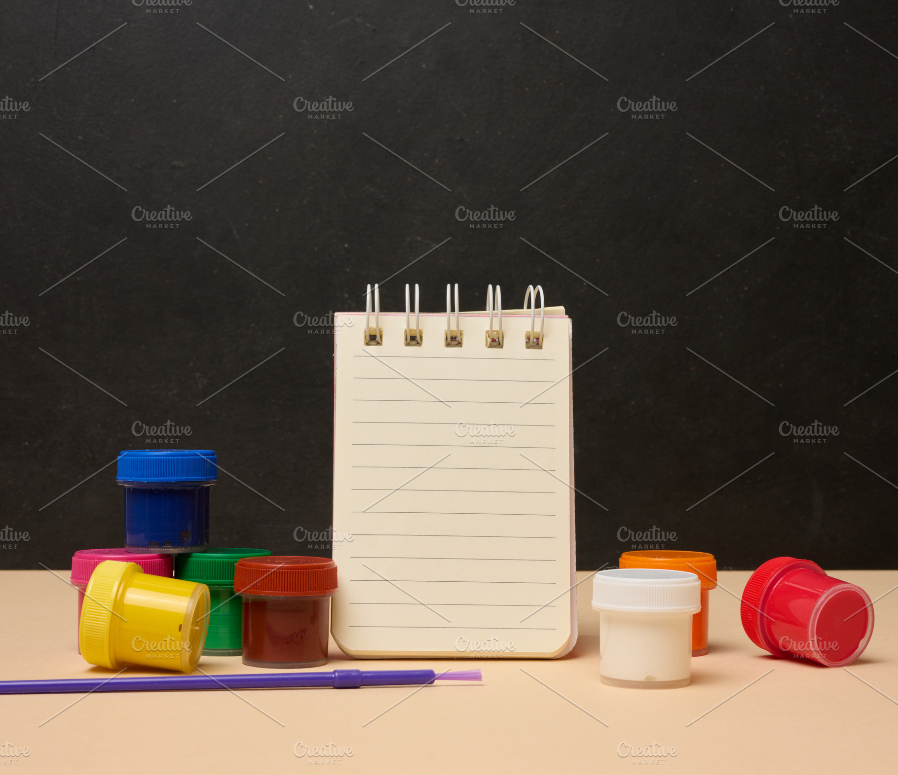 An open white spiral notebook surrounded by colorful paint cans, a School & Education Photo by ndanko