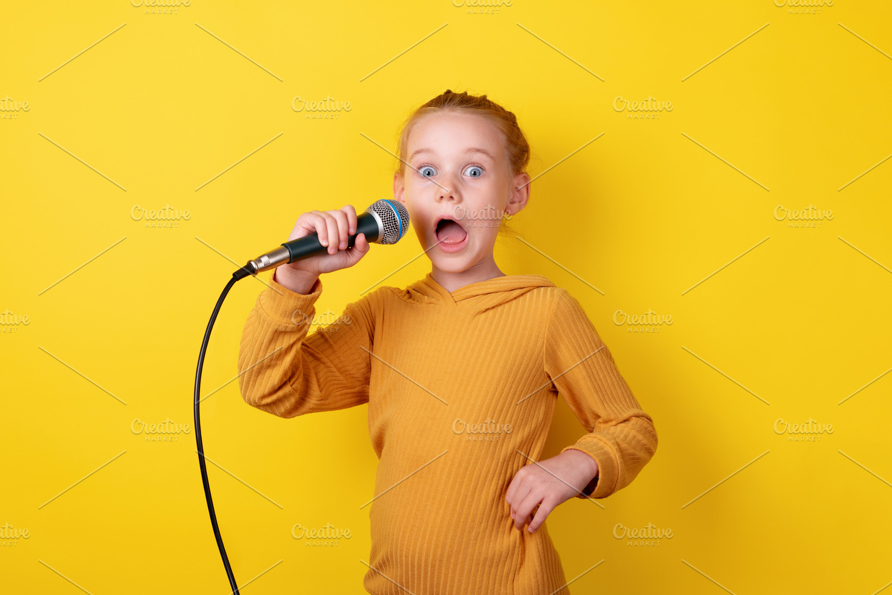 Excited young girl in yellow holding a microphone, singing with, a Person Photo by Ales Munt