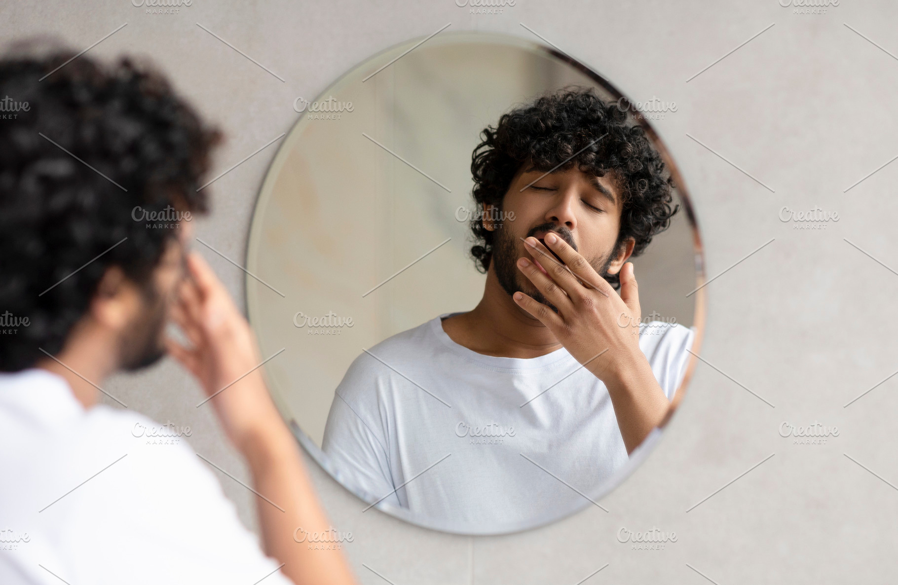 Sleepy indian guy yawning while standing near mirror in bathroom at home, doing, a Person Photo by Prostock-Studio