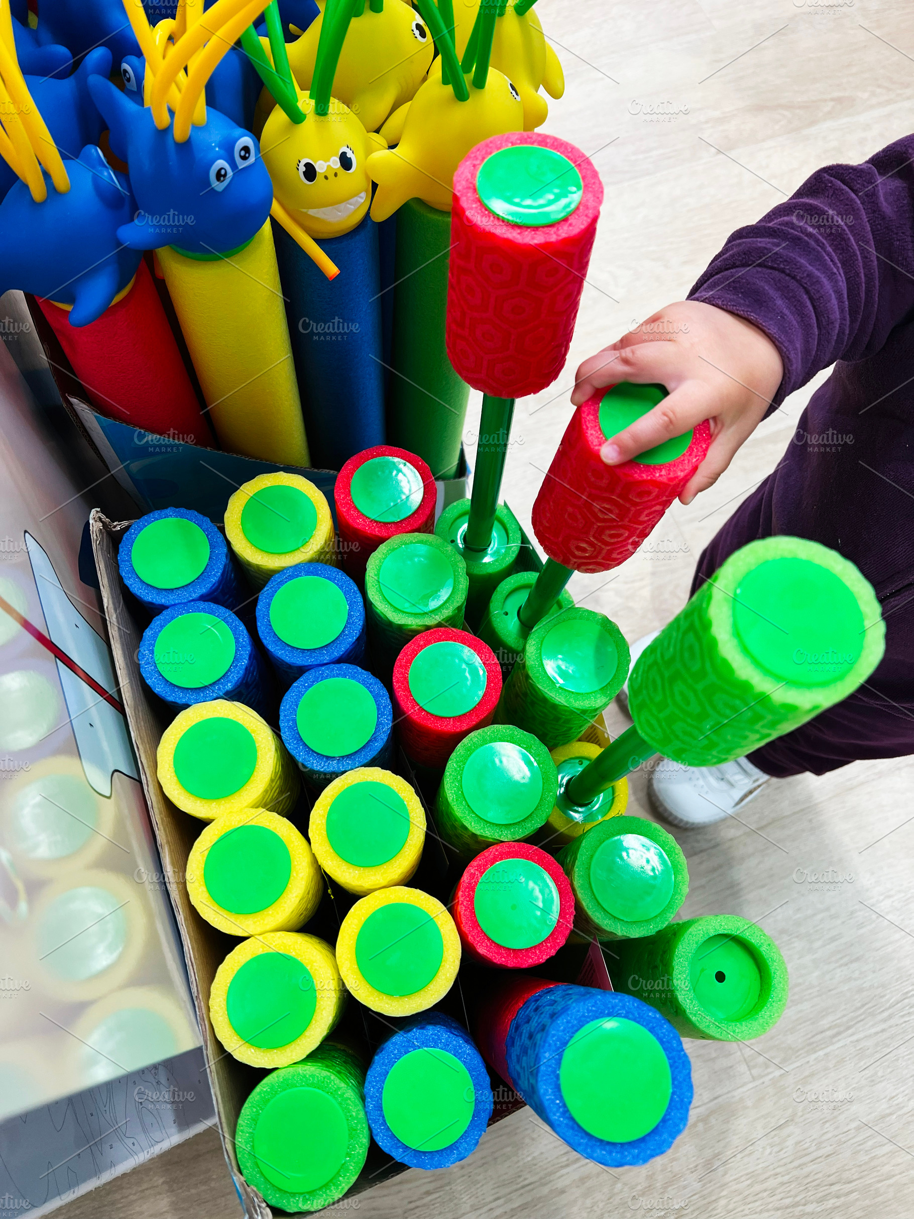 Child selecting colorful pool noodles toys with playful designs on a store shel, a Photo by AS photostudio