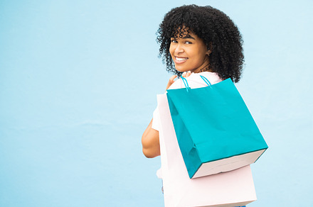Back, portrait and black woman with bags, shopping and purchase expensive items with girl on blue studio background. Mockup, Jamaican female and customer with boutique clothes, retail and discount, a Photo by Peopleimages.com