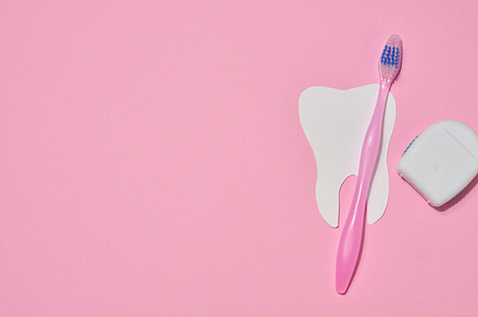 Pink toothbrush, dental floss in a case and a paper cutout tooth