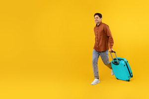 Happy Tourist Guy Walking With Blue Suitcase Over Yellow Background, a Photo by Prostock-Studio