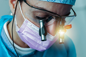 Dentist wearing magnifying glasses and mask performing surgery, a Photo by Antonio Gravante Market