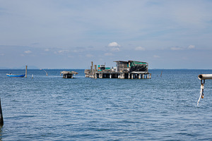 A rustic wooden stilt house and boat with fishing nets, an Architecture Photo by Bepslabor