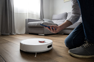 Person controlling robot vacuum cleaner with smartphone in modern living room, a Technology Photo by etorres69