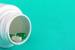White pill bottle tipped over with green and white capsules on turquoise backgr, a Health & Medical Photo by Ales Munt
