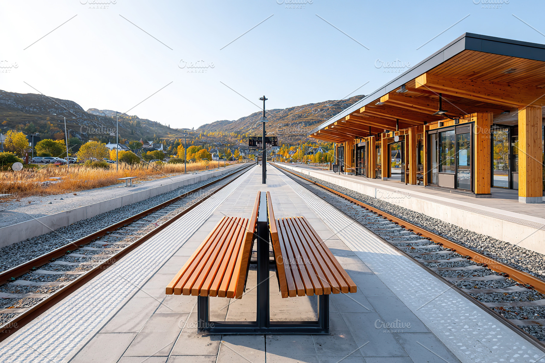 Train station platform with benches and wooden shelter in autumn landscape, a Photo by AlyaAnd