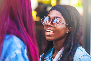 Young black woman wearing sunglasses talking with a friend with vivid hair colo, a Person Photo by Antonio Gravante Market