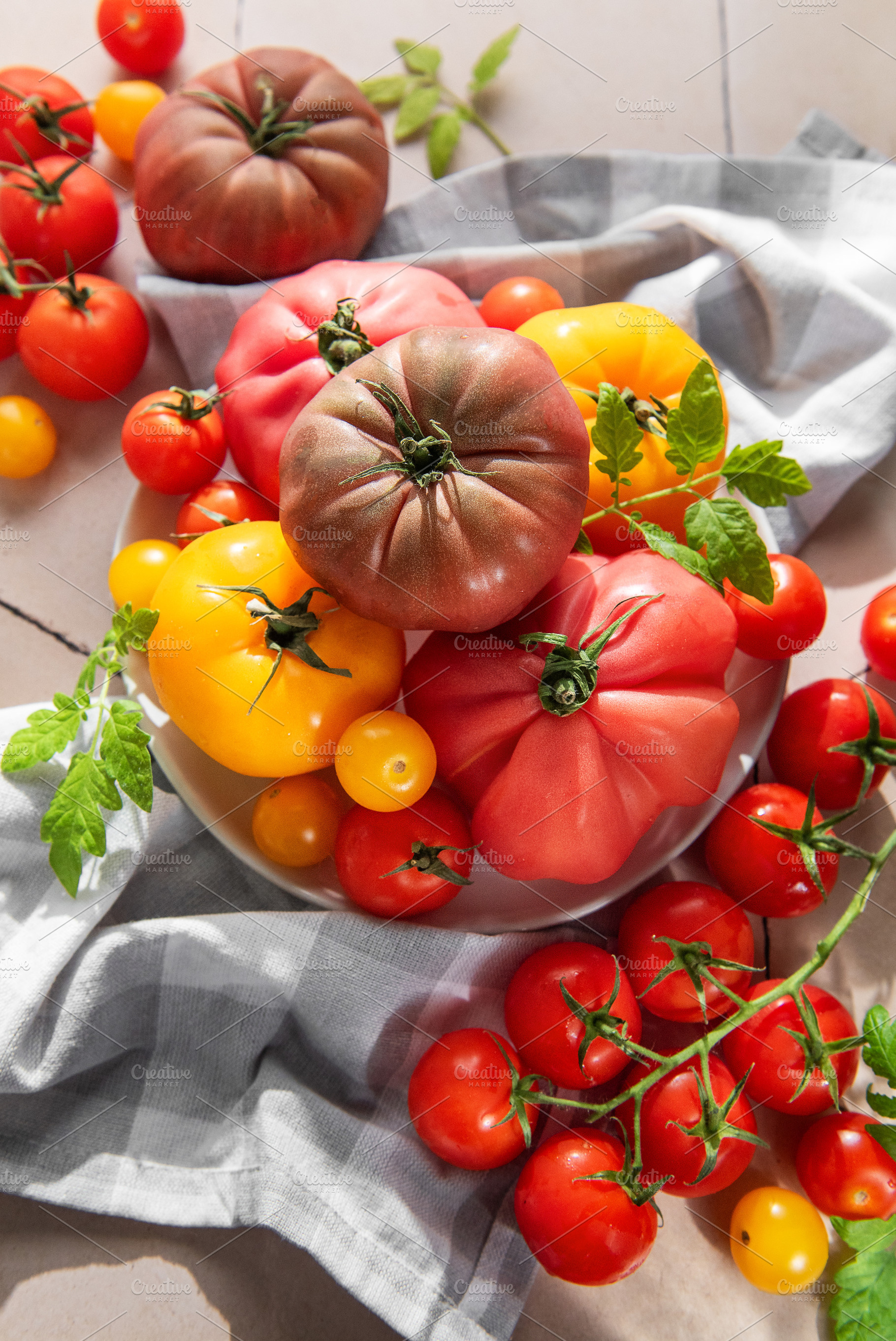Fresh heirloom tomatoes and cherry tomatoes on tile surface, a Food & Drink Photo by Olena Rudo