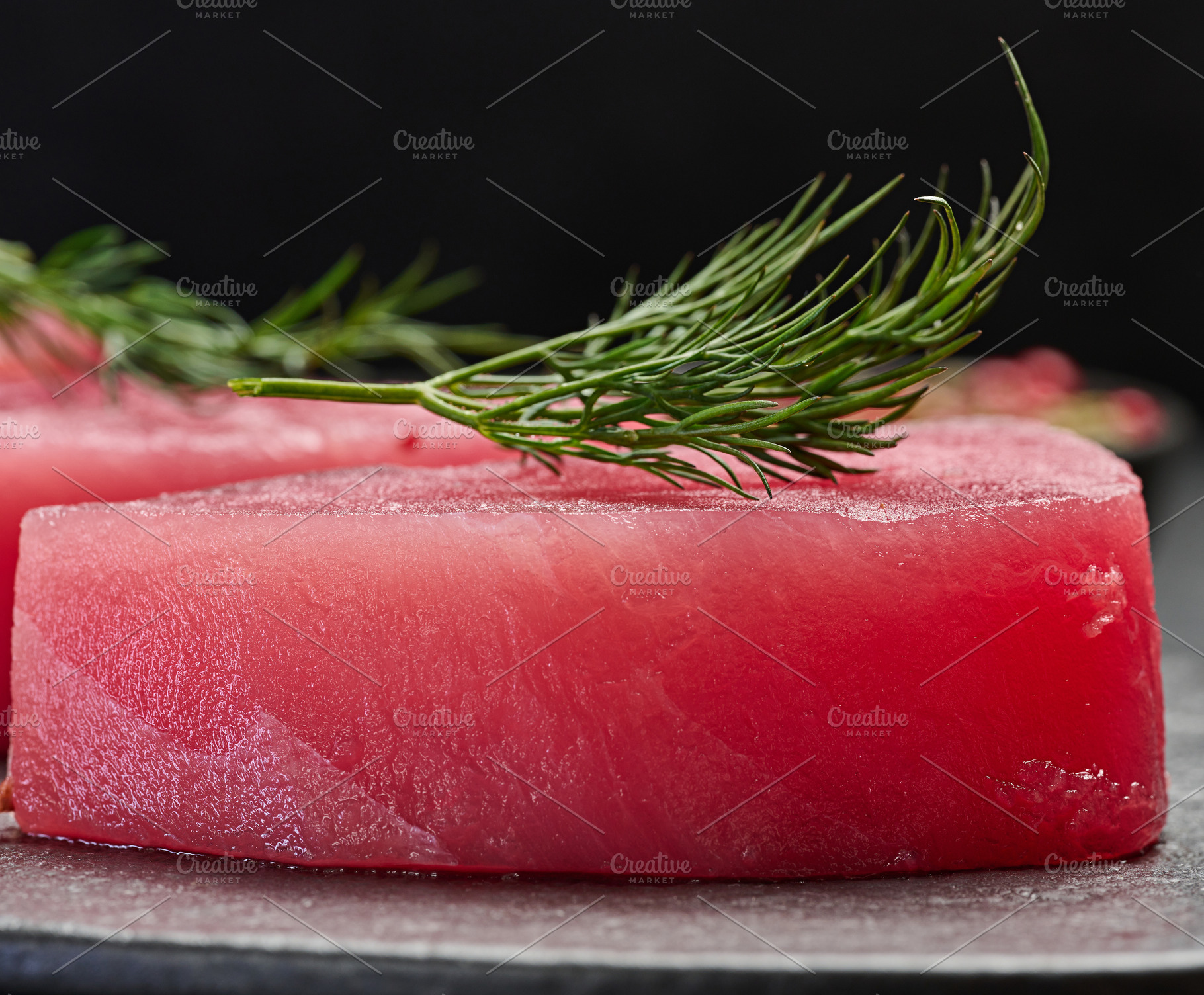 Raw piece of tuna with a sprig of dill on a black board, close u, a Food & Drink Photo by ndanko