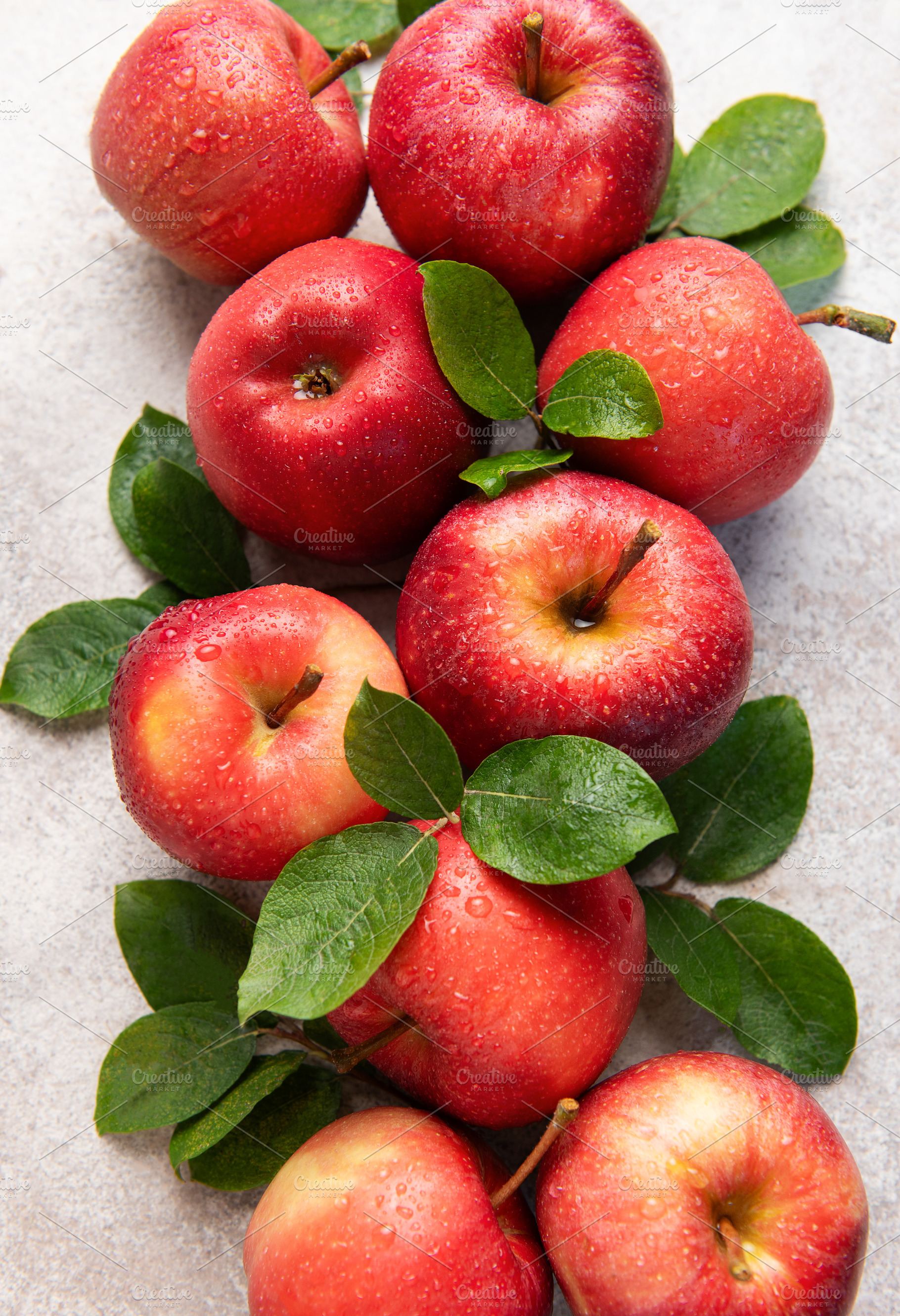 Fresh red apples with green leaves resting on gray surface, a Food & Drink Photo by Olena Rudo