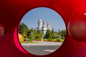 White church with twin towers framed through a bold red circular sculpture, sur, a Person Photo by Ales Munt
