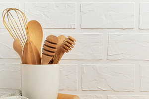 Kitchen utensils resting on wooden countertop by white brick wal, a Food & Drink Photo by Olena Rudo