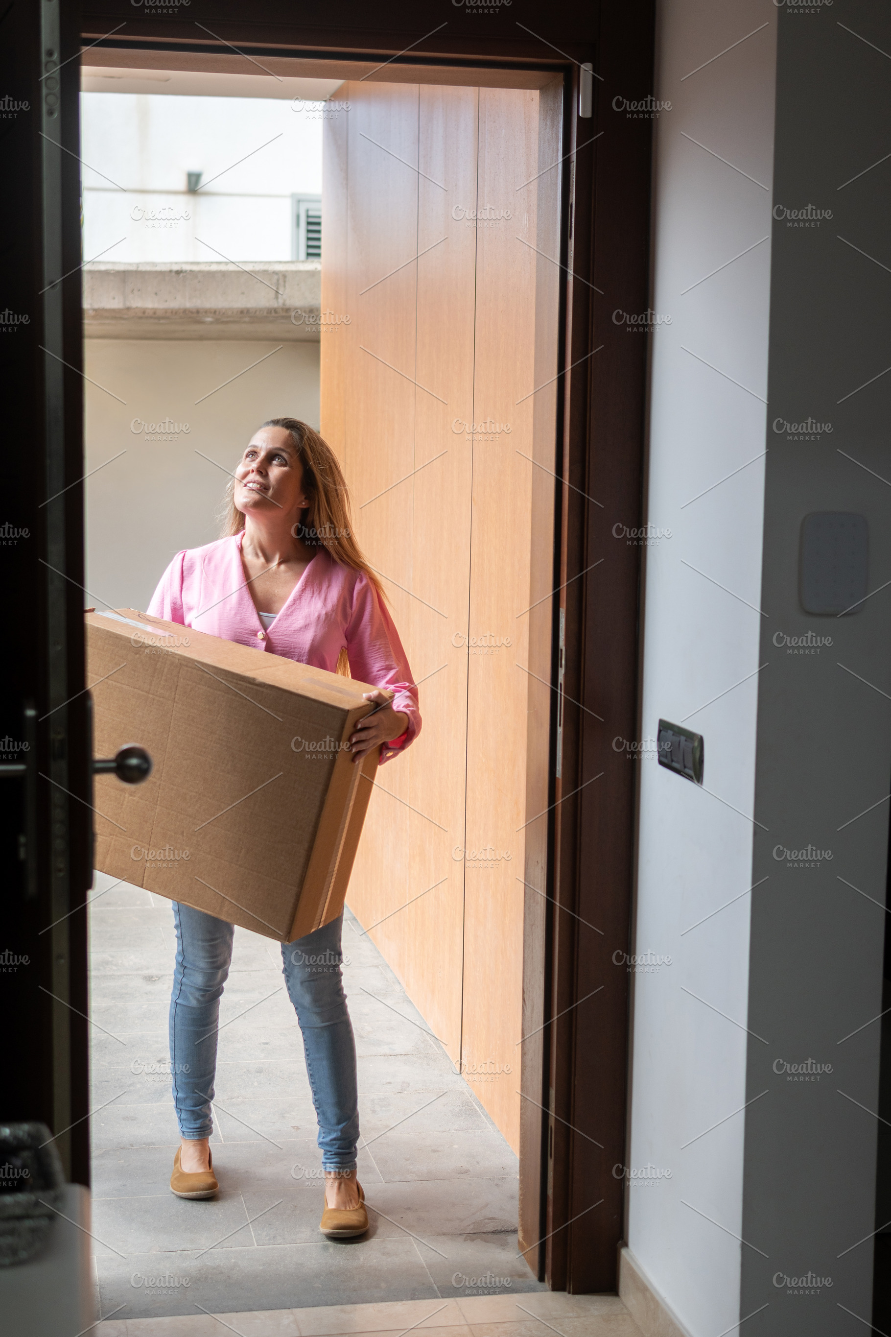 Woman carrying moving box into new home through front door, a Person Photo by etorres69