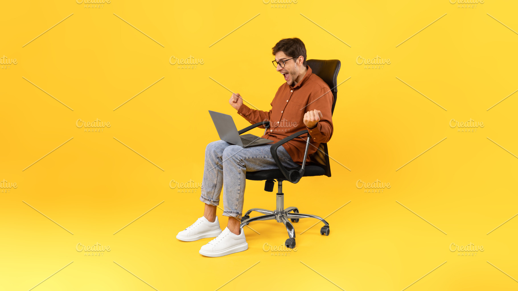 Joyful Guy Shaking Fists Using Laptop Sitting Over Yellow Background, a Photo by Prostock-Studio