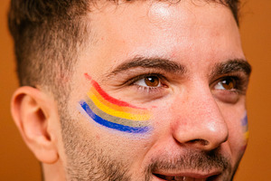 Young man with rainbow face paint celebrating pride, a Photo by karrastock