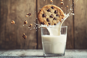 Chocolate cookie falling into glass with white milk, a Food & Drink Photo by AlyaAnd