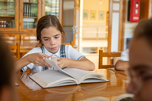 Focused Schoolgirl Reading a Book in School Library During Study Time, a School & Education Photo by etorres69