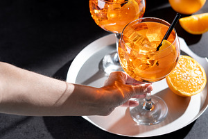 Woman holding refreshing Aperol Spritz cocktail with orange slices and ice, a Food & Drink Photo by etorres69