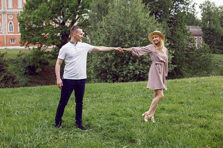 man and a woman in love in a dress and hat are walk on a green field under a tr, a Person Photo by SaulichPhoto