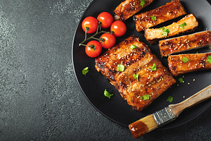 Hot grilled spare ribs from a summer BBQ served on a plate with sauce. Top view, a Food & Drink Photo by Budarinphoto
