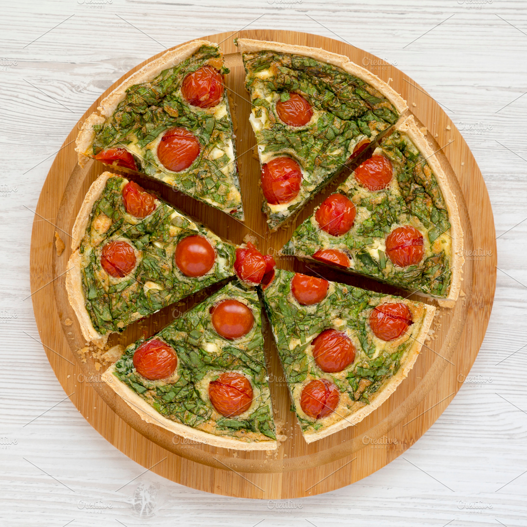 Homemade Spinach Quiche on a round bamboo board, top view. Flat, a Food & Drink Photo by LiudmylaChuhunova