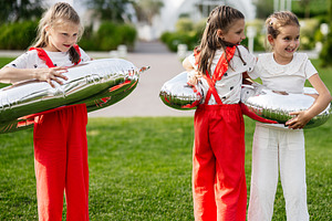 Three children playing with shiny balloons outdoors on a sunny day, a Photo by AS photostudio