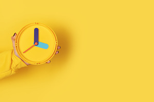 Minimalist yellow clock held by hand on solid yellow background,, a Holiday Photo by Ales Munt