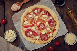 Pizza with salami, ham and mozzarella cheese on a wooden table, a Food & Drink Photo by ndanko